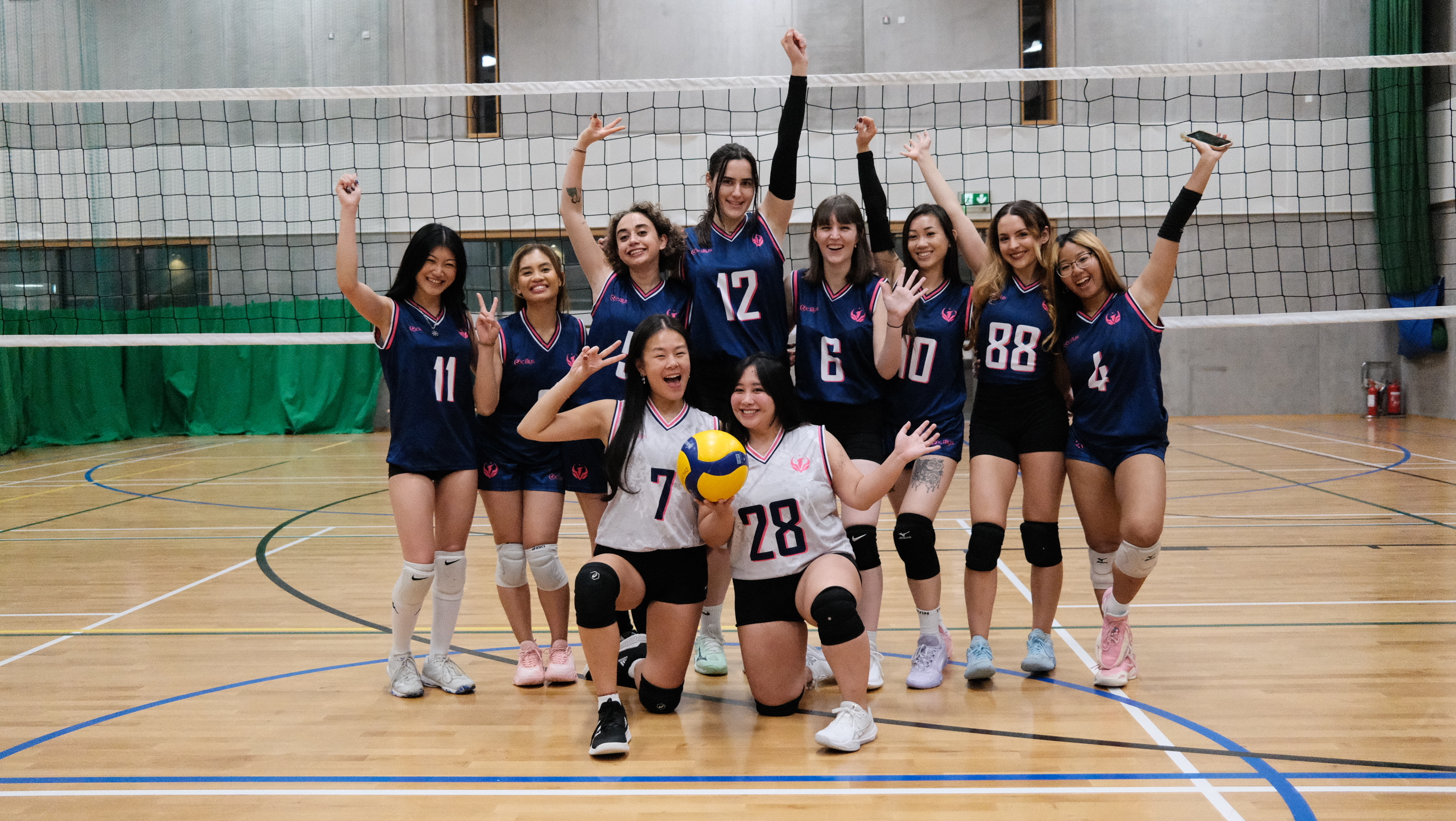 Celestials Women’s Division 3 squad together on the volleyball court in their navy and white kits with pink accents.